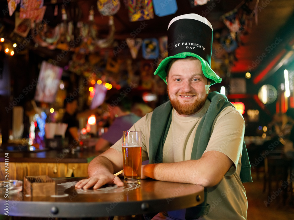 A smiling happy man in a leprechaun hat with beer in pub. He celebrates St. Patrick