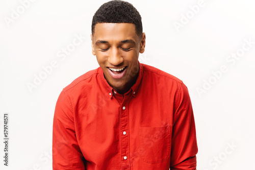 Headshot of friendly optimistic African-American guy in red shirt isolated on white. Smiling kind male student looking down, portrait of employee