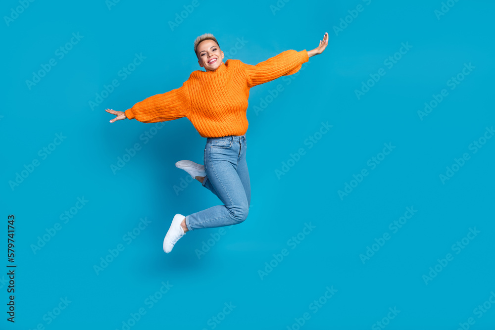 Full length photo of carefree shiny dressed knitted pullover jumping high arms sides empty space isolated blue color background