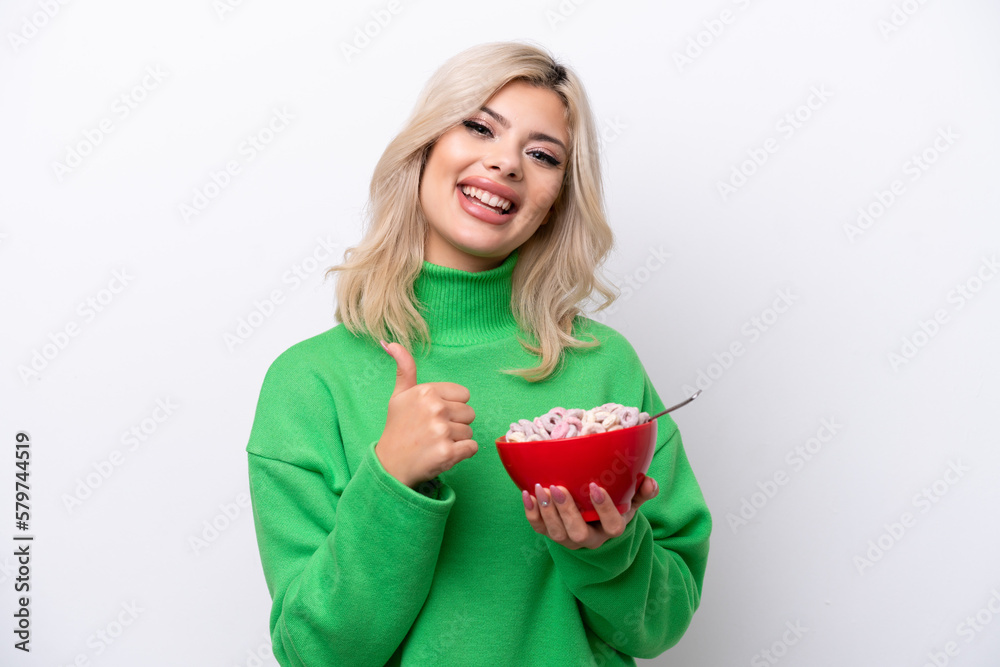 Young Russian woman holding a bowl of cereals isolated on white background giving a thumbs up gesture Young Russian woman holding a bowl of cereals isolated on white background giving a thumbs up gesture