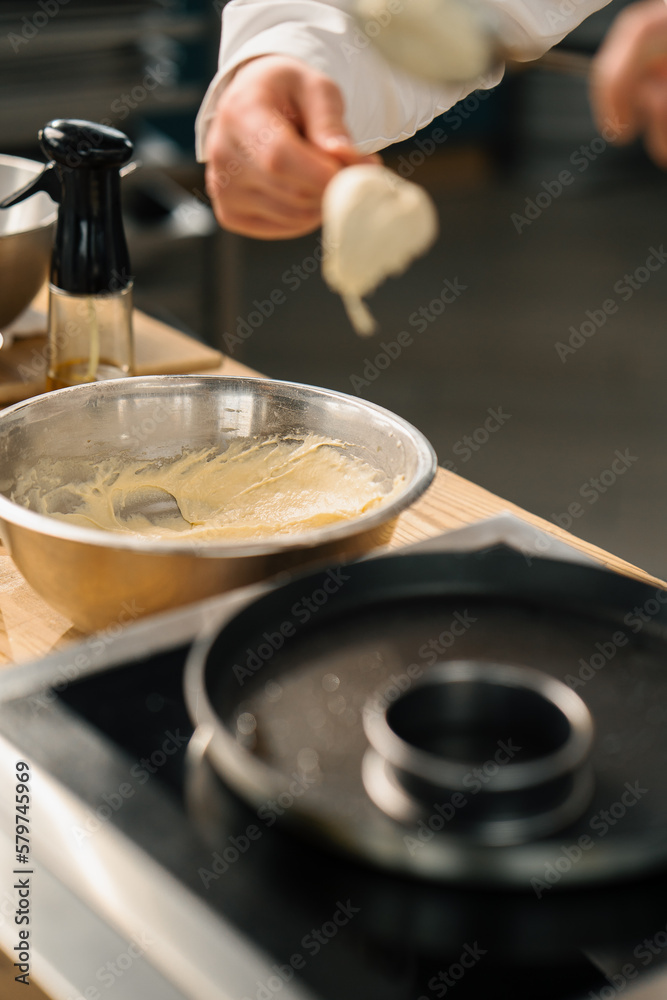A professional chef in the kitchen of a restaurant prepares pancakes for breakfast. Culinary recipe Frying pan on the stove