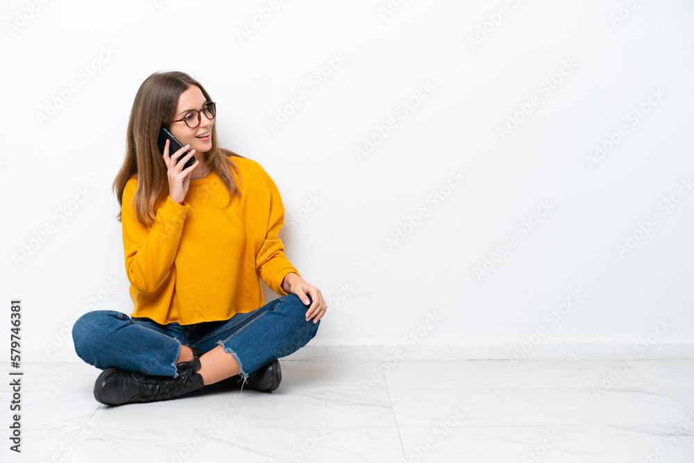 Young caucasian woman sitting on the floor isolated on white background keeping a conversation with the mobile phone with someone Young caucasian woman sitting on the floor isolated on white background keeping a conversation with the mobile phone with someone