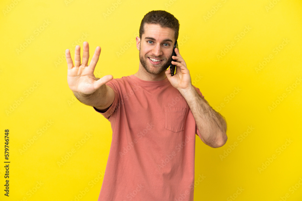 Handsome blonde man using mobile phone over isolated background counting five with fingers