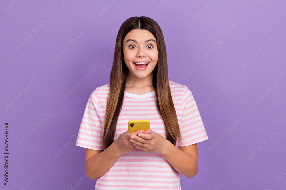 Photo of impressed funny girl dressed striped white pink t-shirt typing modern device isolated purple color background Photo of impressed funny girl dressed striped white pink t-shirt typing modern device isolated purple color background