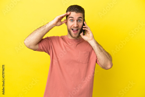 Handsome blonde man using mobile phone over isolated background with surprise expression