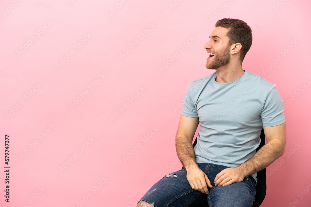 Fototapeta premium Young man sitting on a chair over isolated pink background laughing in lateral position