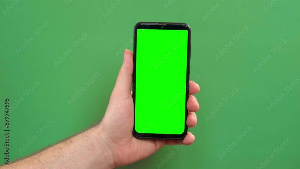Mobile phone in young man hand. Use smartphone with blank green screen on green color studio background. Male showing black phone with chroma key display. Close up. Mock up of smart phone for Ad, app Mobile phone in young man hand. Use smartphone with blank green screen on green color studio background. Male showing black phone with chroma key display. Close up. Mock up of smart phone for Ad, app