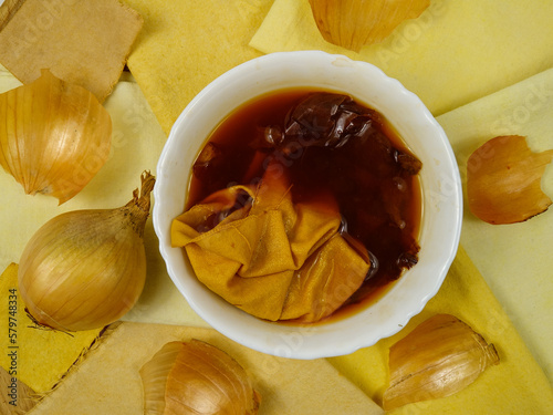 Bowl with decoction of onion husks and samples of cotton fabric with gradient in yellow tones, background.  Natural dyeing for fabrics, DIY
 photo