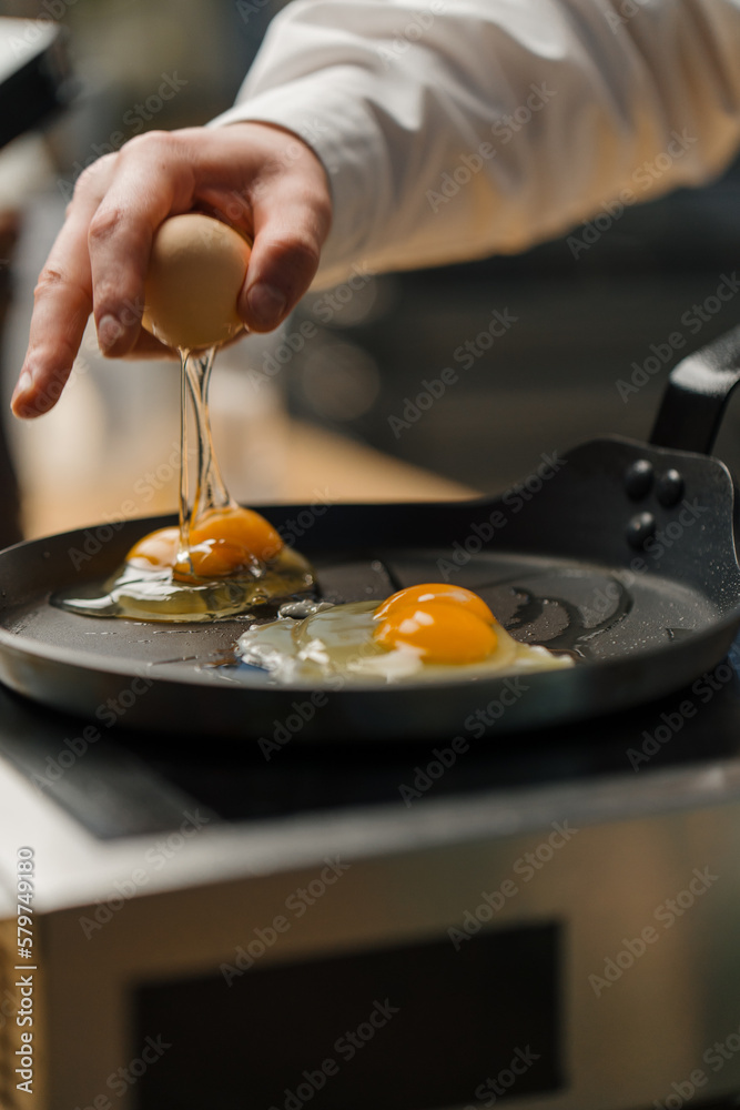 Fototapeta premium A cook breaks an egg into a pan Preparing breakfast in a professional kitchen