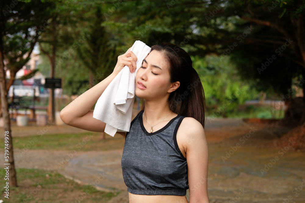 Beautiful young Asian woman wiping off her sweat after her morning exercise at a running track on a brtight sunny morning Beautiful young Asian woman wiping off her sweat after her morning exercise at a running track on a brtight sunny morning