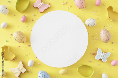 Easter decoration idea. Flat lay photo of white circle colorful eggs butterfly shaped cookies sprinkles and baking molds on isolated yellow background with blank space