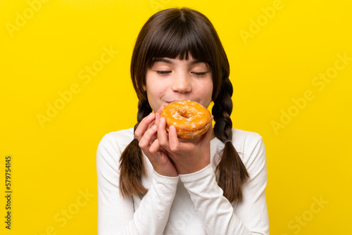Little caucasian girl isolated on yellow background holding a donut