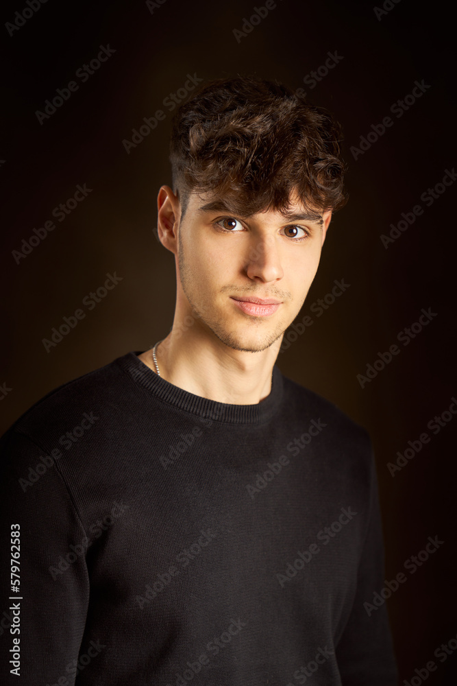 Teen boy standing against dark brown background Teen boy standing against dark brown background
