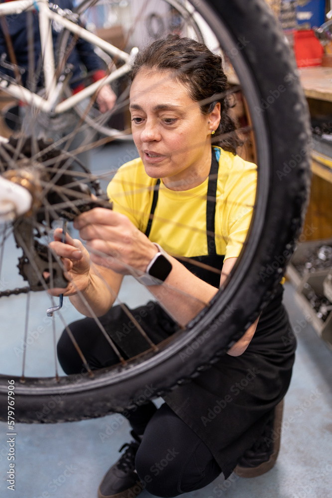 Φωτογραφία Woman fixing bike gearbox in self-repair shop, vertical photo where the girl bending down with the bike hanging adjusting the rear wheel parts