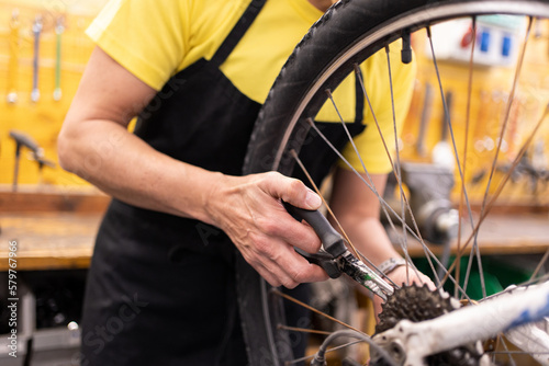 detail of woman's hand with pliers fixing bike, unrecognizable girl with black apron and yellow t-shirt adjusting bike parts