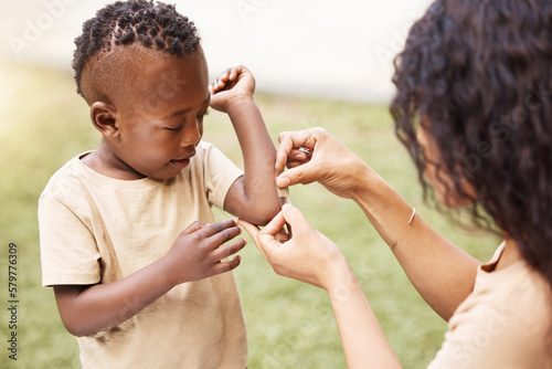 It wont hurt anymore. Shot of a mother applying a bandaid to her sons arm outside. photo