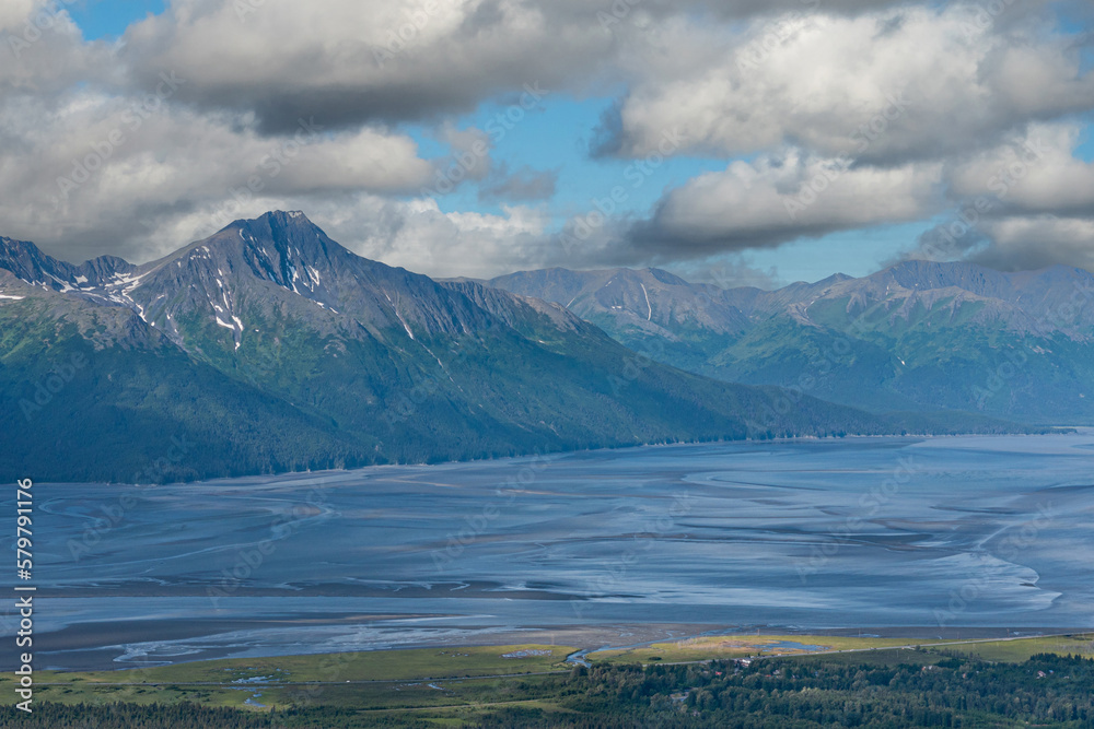 Girdwood Alaska, USA - July 23, 2011: Wide landscape shows blue sandy Turmagain Arm ocean connection in front of tall gray-green mountain range and green forested valley up front