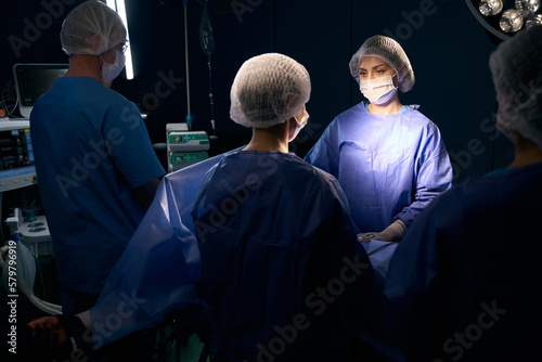 Group of people in surgical overalls stand at operating table