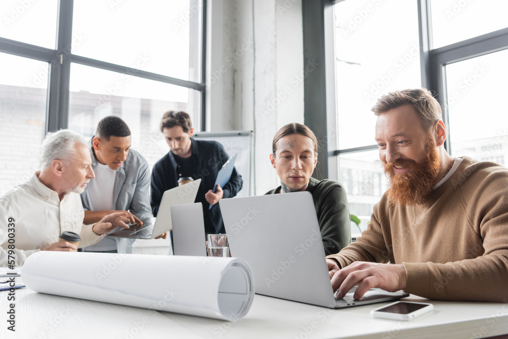 Smiling businessman using laptop near colleagues during business meeting in office.