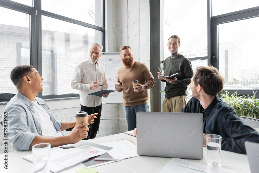 Cheerful business people talking to interracial colleagues with clipboard during training in office. Cheerful business people talking to interracial colleagues with clipboard during training in office.