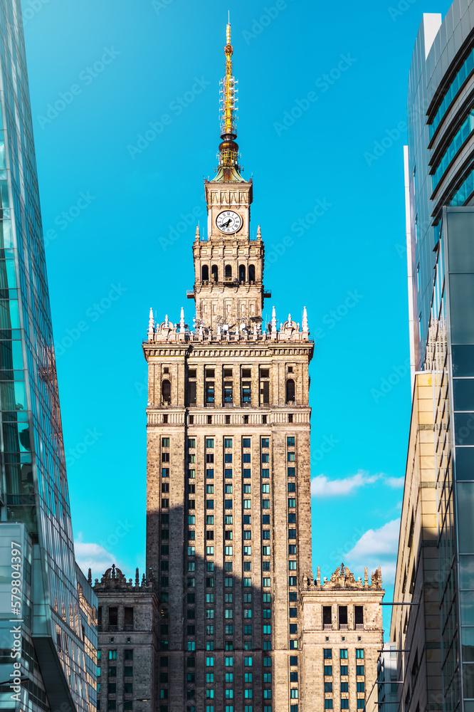 Obraz premium The clock tower of the Palace of Culture and Science,a historical symbol of Warsaw in the Empire style, surrounded by modern buildings.A combination of styles in the architectural appearance.Vertical