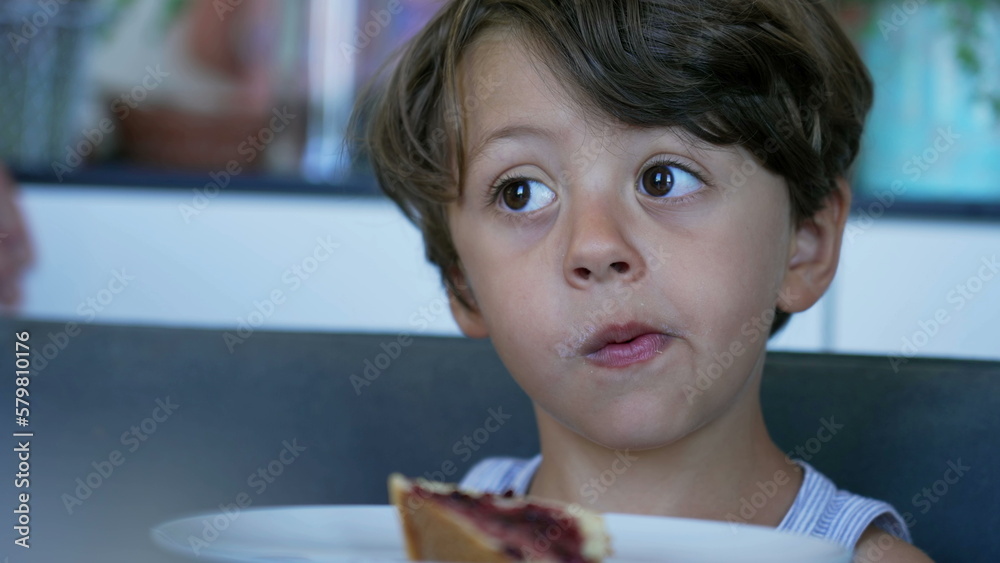 Child eating bread with jelly in morning breafast table. Candid small ...