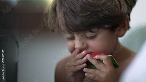 Candid child taking a bite of red watermelon fruit. One small boy eating healthy fruit