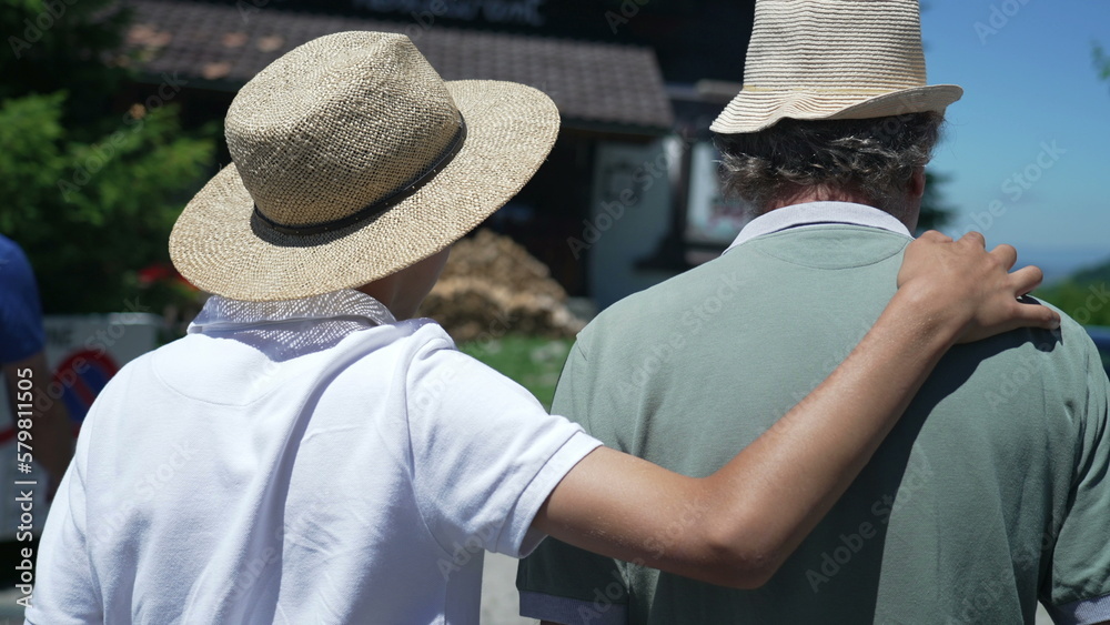 Back of son embracing father with arm around walking outside together wearing Panama Hats during sunny beautiful day