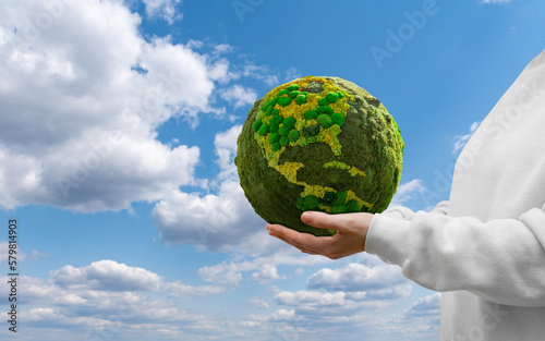Fototapeta Naklejka Na Ścianę i Meble -  Woman holds a green planet Earth on a background of blue sky. Symbol of sustainable development and renewable energy	