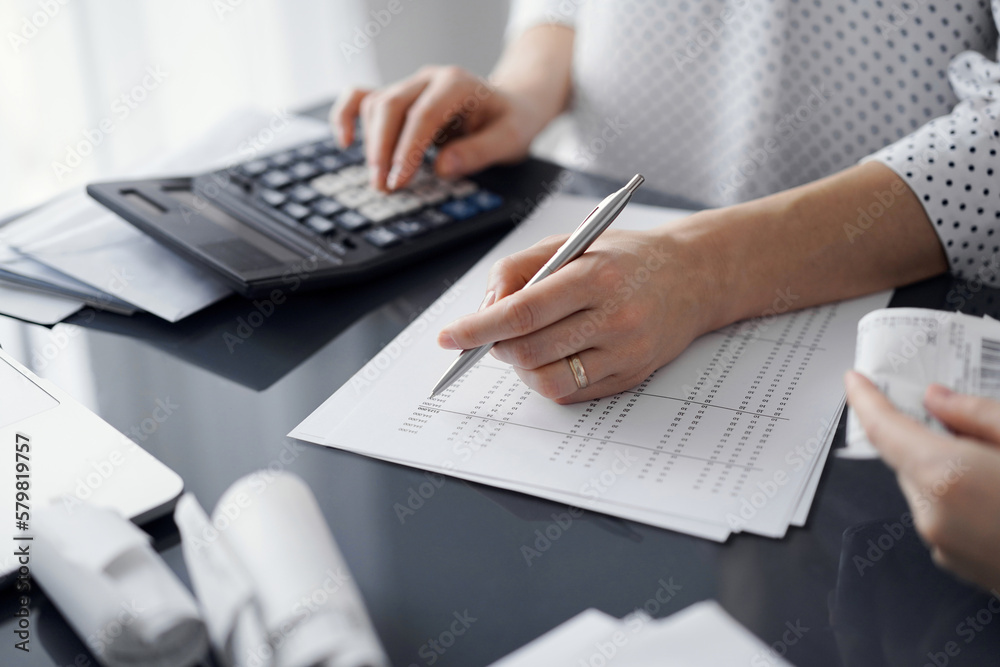 Woman accountant using a calculator and laptop computer while counting taxes for a client. Business audit and finance concepts.