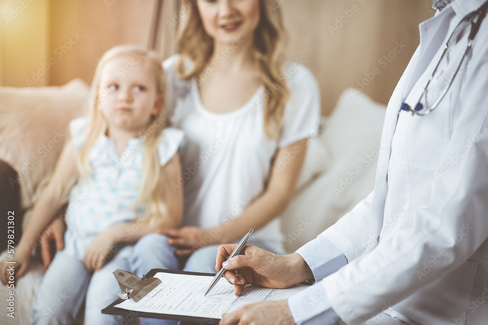 Doctor and patient. Pediatrician using clipboard while examining little girl with her mother at home. Sick and unhappy child at medical exam Doctor and patient. Pediatrician using clipboard while examining little girl with her mother at home. Sick and unhappy child at medical exam