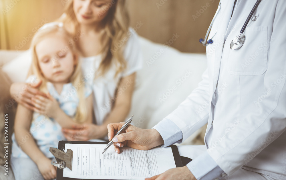 Obraz premium Doctor and patient. Pediatrician using clipboard while examining little girl with her mother at home. Sick and unhappy child at medical exam