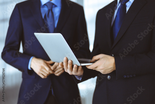 Business people discussing a presentation at meeting, standing in a modern office. Unknown businessman with a colleague search for some information at the laptop, lawyers at negotiation