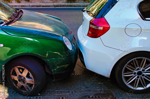 Two cars are parked very close. Two cars next to each other. Small clearance between car bumpers. Problems with parking in big cities. Car parking in European city. Valencia, Spain