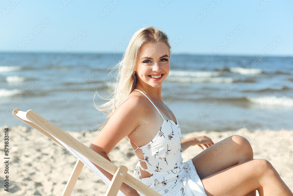 Happy blonde woman relaxing on a wooden deck chair at the ocean beach.
