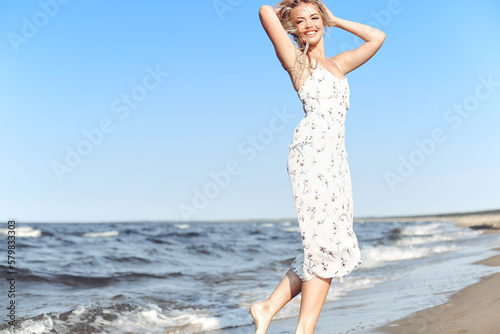 Happy blonde beautiful woman having fun on ocean beach while dancing in waves.