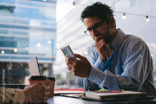 Middle-aged man in a coffee shop looking at his cell phone in wonder.