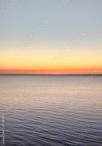  Sunset background of light horizon peach warm sky with water. Natural light orange sunset sky background with ocean.