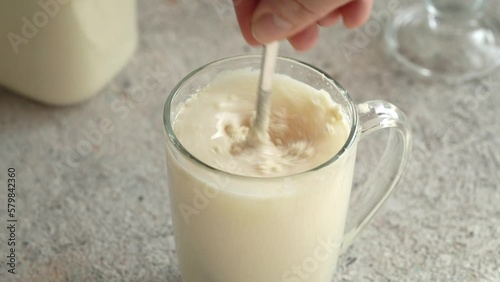 Hand stirring whey protein powder in a glass of water on a table