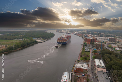 aerial shot of a container ship sailing along the Savannah River surrounded by hotels, office buildings, restaurants and lush green trees along the banks with cars on the street in Savannah Georgia photo