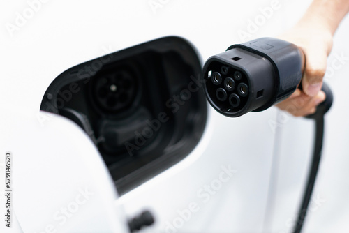 Progressive new alternative clean energy vehicle and electric charging device concept. Focus closeup hand holding and pointing EV charger plug at camear from electric charging station at camera photo