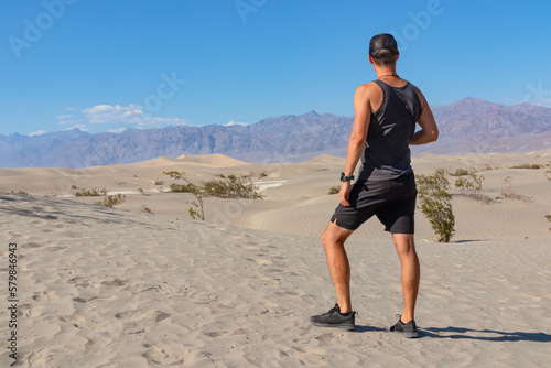 Rear view of man looking at Mesquite Flat Sand Dunes in Death Valley National Park, California, USA. Panoramic view on dry Mojave desert on sunny summer day with Amargosa Mountain Range in the back