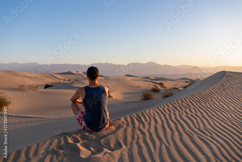 Touristic man enjoying the sunrise with scenic view on Mesquite Flat Sand Dunes, Death Valley National Park, California, USA. Morning walk in Mojave desert with Amargosa Mountain Range in back. photo