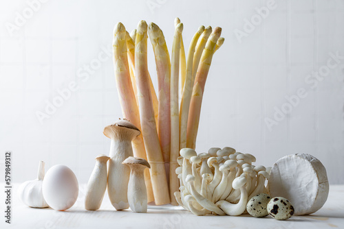 Bunch of raw white asparagus in a jar and mushrooms on wooden table. White food ingredients still life