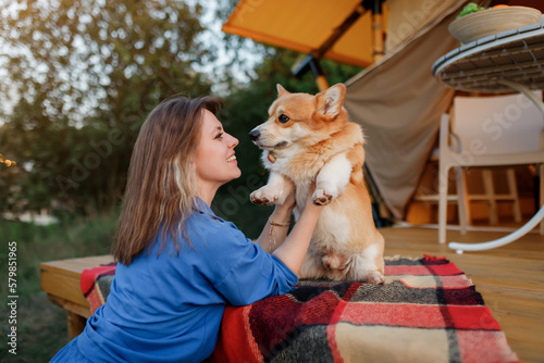 Happy young woman with Welsh Corgi Pembroke dog relaxing in glamping on summer day. Luxury camping tent for outdoor recreation and recreation. Lifestyle concept