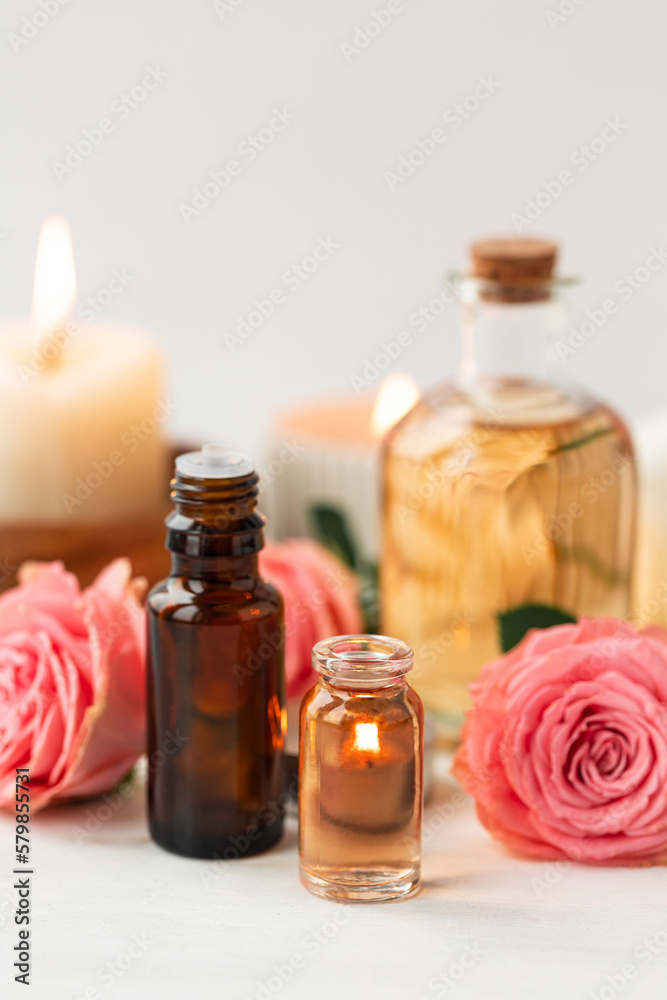 Aromatherapy. Concept of pure organic essential rose oil. Elixir with plant based floral or herbal ingredients. Pink flowers extract. Spa atmosphere with candle, towel. White background Aromatherapy. Concept of pure organic essential rose oil. Elixir with plant based floral or herbal ingredients. Pink flowers extract. Spa atmosphere with candle, towel. White background
