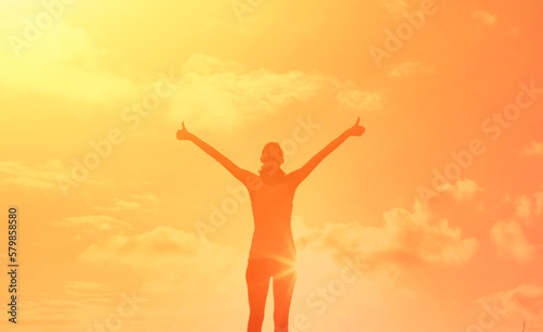 Young female feeling grateful, positive, joyful standing outdoors in the sunrise 