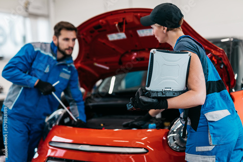 Male and female mechanics working together in large modern car repair service.