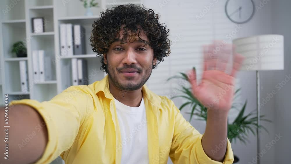 POV Cheerful office worker talking on video call smartphone front camera view standing in office at workplace Employee holding phone in hand taking selfie speaking Indoors, looking at camera smiling