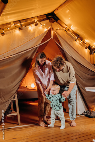 Happy family with lovely baby relaxing and spend time together in glamping on summer evening. Luxury camping tent for outdoor recreation and recreation. Lifestyle concept © bondvit